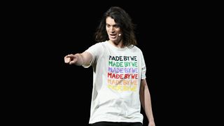 Adam Neumann, in a white t-shirt that says "MADE BY WE," points at an audience member from stage. 
